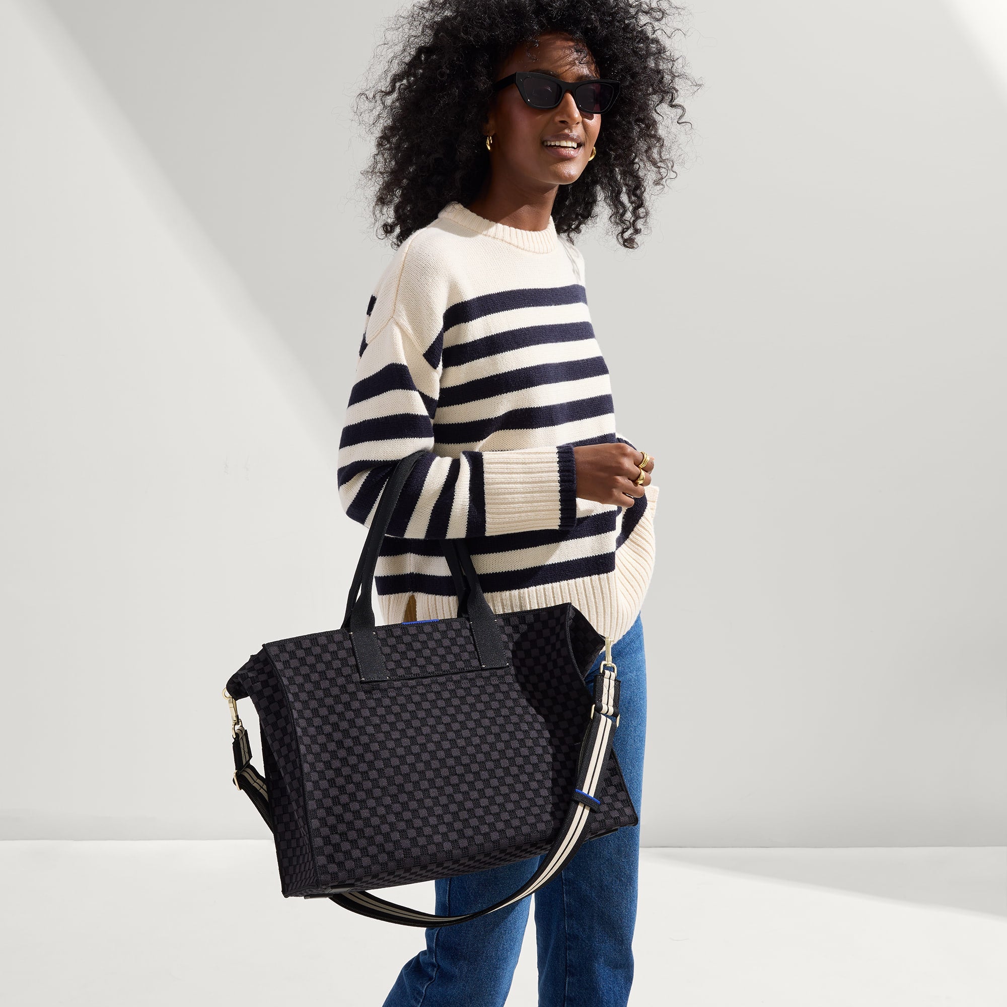 The Classic Tote in Black Sand, carried by its top handles by a model, shown from side.