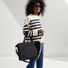 The Classic Tote in Black Sand, carried by its top handles by a model, shown from side.